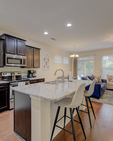 Open-plan kitchen and living room with dark wood cabinets, granite island, stainless steel appliances, and seating area with blue sofa.