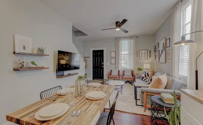 Bright dining and living room with wood table, gallery wall, large windows, and warm natural light